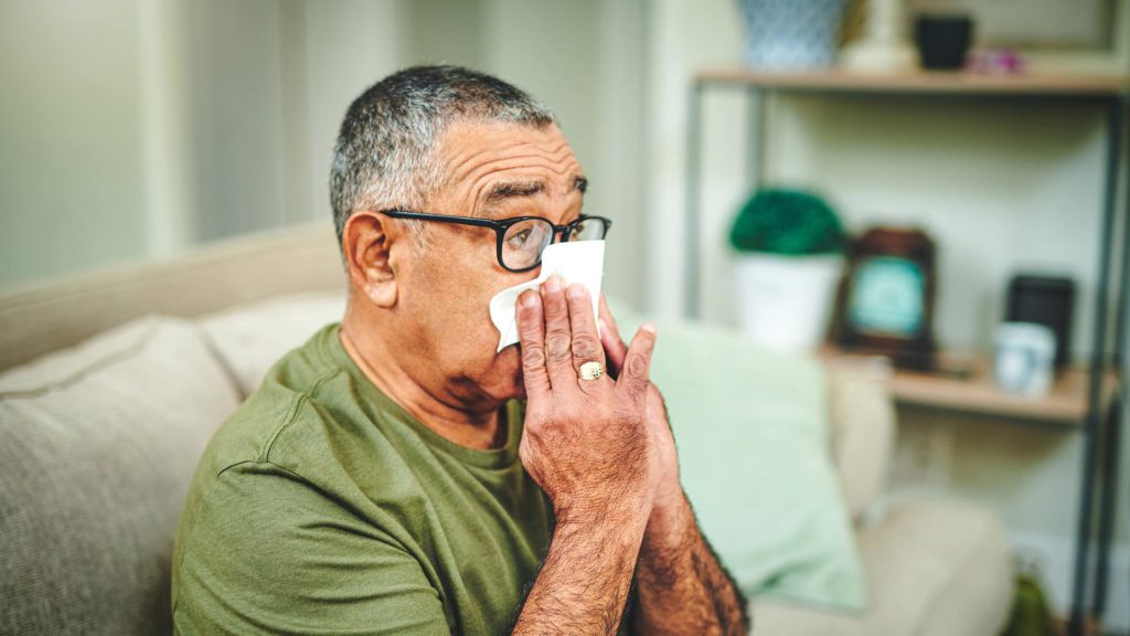 Older man blowing nose because of cold or flu symptoms