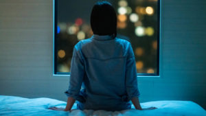 woman sitting on bed staring out a window at midnight