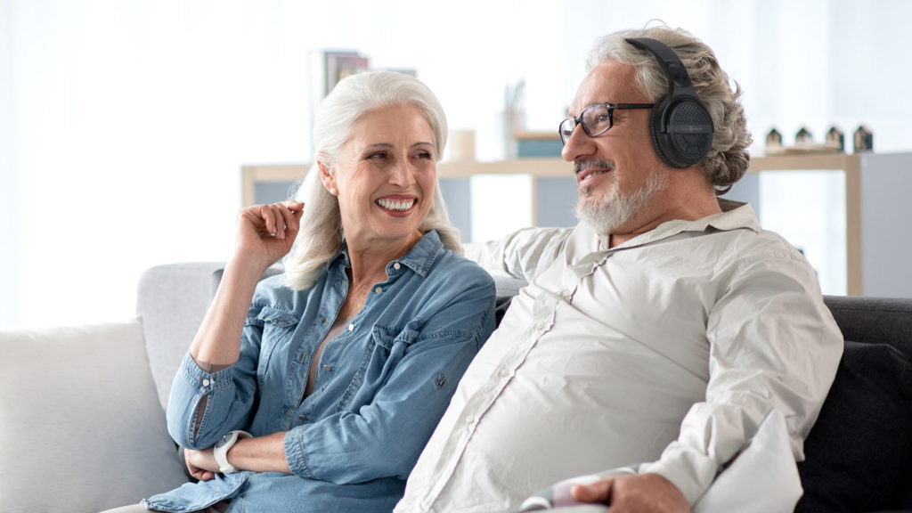 Older man watching TV with his partner while using AudioRange OTE-1000 Wireless TV Headphones