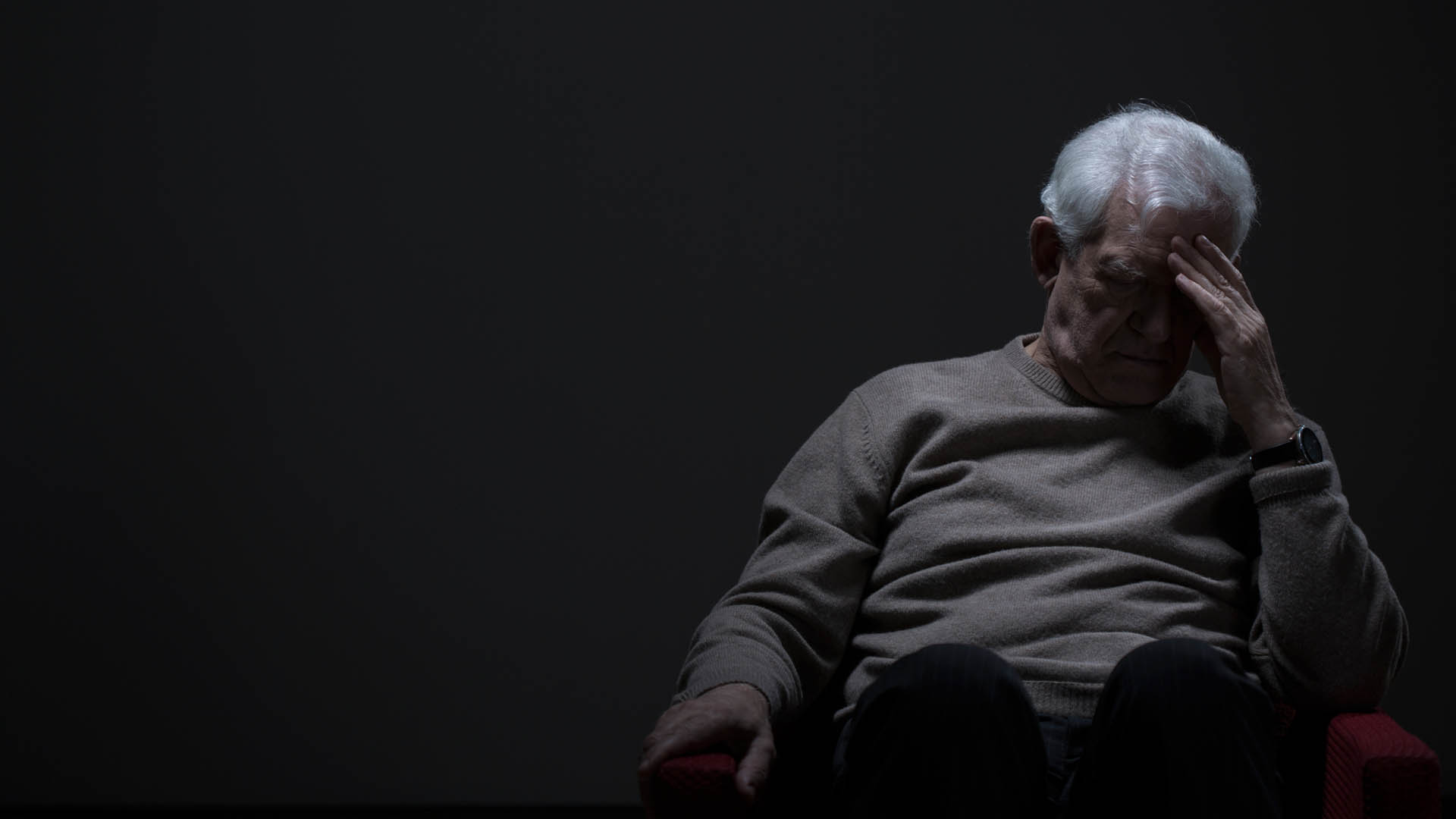 man sitting in dark room with head in hands