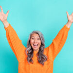 Portrait of attractive amazed grey-haired woman rising hands up having fun rejoicing isolated over bright teal turquoise color background